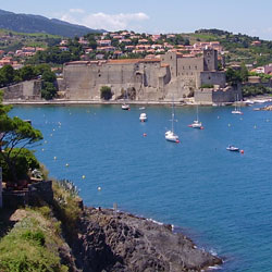 Imagen de Collioure, pueblo de sur de Francia. Se ve el mar, el castillo al borde del mar, y casas en la montaña, y la montaña.