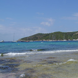 Vista de la playa de Las-Salinas, de Ibiza. Al fondo se ve un brazo de costa, verde, rodeado del azul del cielo y del mar.